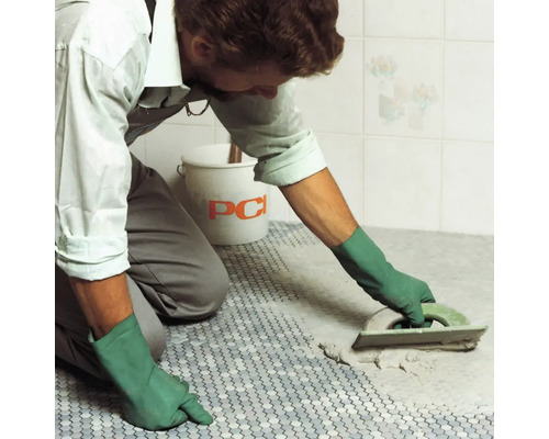 Un artisan joint des carreaux de mosaïque avec une taloche à joints, un seau de la société PCI est visible à l''arrière-plan.