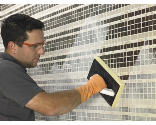 Une personne joint des carreaux de mosaïque avec une taloche à joints.