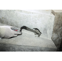 Une main gantée bouche un trou dans un escalier en béton avec une truelle et du mortier de jointoiement.