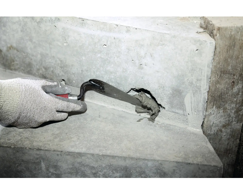Une main gantée bouche un trou dans un escalier en béton avec une truelle et du mortier de jointoiement.
