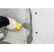 Un artisan remplit une fissure dans un mur en béton avec du mastic