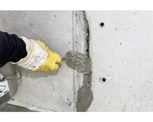 Un artisan remplit une fissure dans un mur en béton avec du mastic