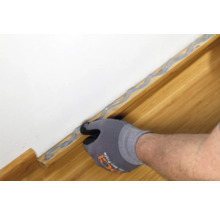 Handwerker versiegelt Fugen zwischen Wand und Sockelleiste mit Dichtstoff.