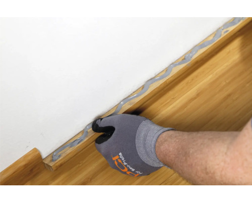 Un artisan scelle les joints entre le mur et la plinthe avec du mastic.