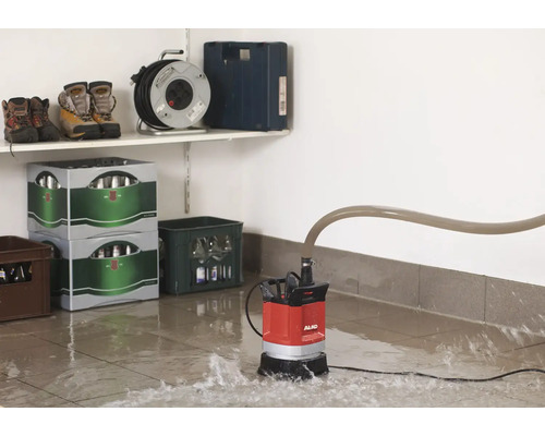 Rote Tauchpumpe von AL-KO im Einsatz auf einem gefluteten Boden, mit Gegenständen im Hintergrund