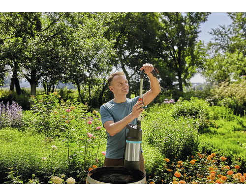 Ein Mann bedient eine Tauchdruckpumpe in einem Garten, um Wasser aus einem Fass zu pumpen.