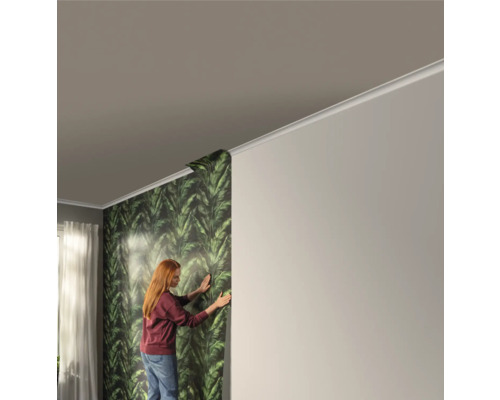 Frau tapeziert eine Wand mit einer grünen Blättertapete in einem Raum.