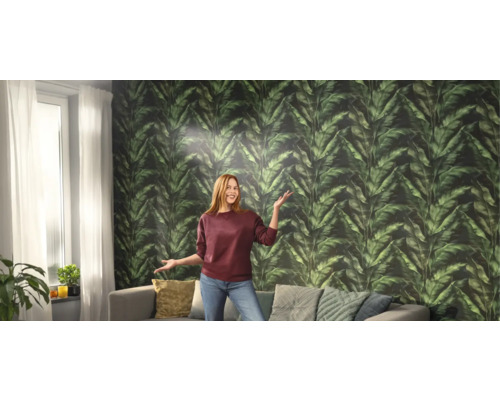 Wohnzimmer mit Blattmuster-Tapete, Sofa und einer Frau.