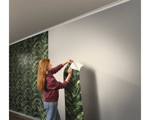 Une femme pose du papier peint à feuilles vertes sur le mur