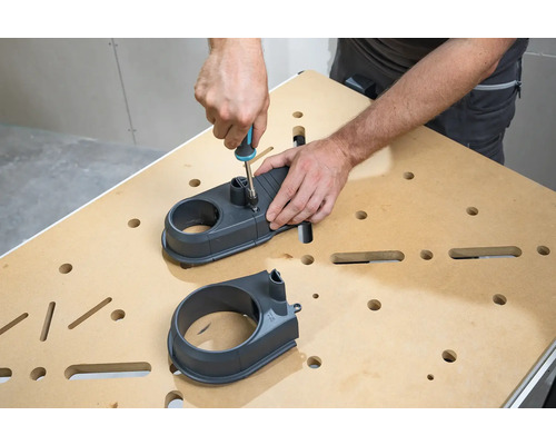 Person montiert Absaugstutzen mit Schraubenzieher an einer Werkbank