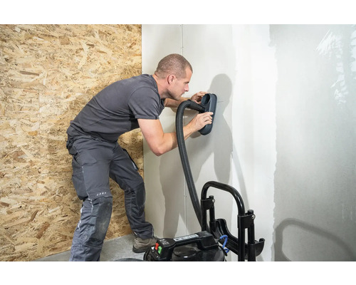 Mann schleift Wand mit Schleifgerät und Staubsauger