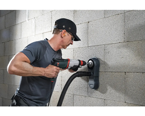Mann bohrt mit einer Bohrmaschine und Staubabsaugung in eine Wand.