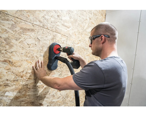 Handwerker bohrt mit einer Bohrmaschine durch eine Holzplatte mit Staubabsaugung