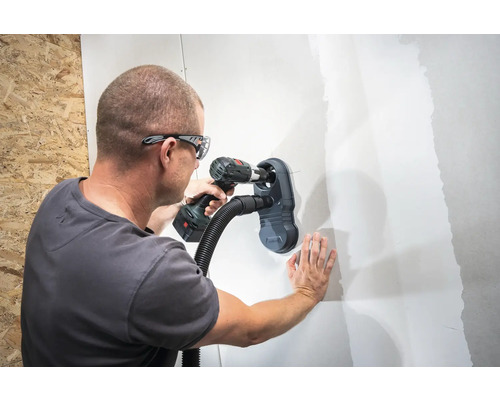 Ein Mann bohrt mit einem Staubsaugeraufsatz ein Loch in eine Wand