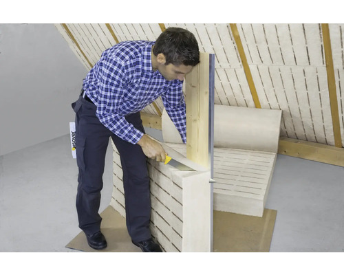 Un homme coupe de la laine isolante avec un couteau dans un grenier.