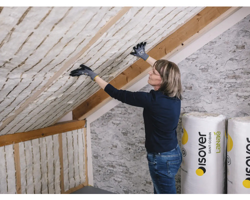 Isolation de toit avec une femme posant de la laine isolante, des chevrons en bois et des rouleaux de la marque Isover