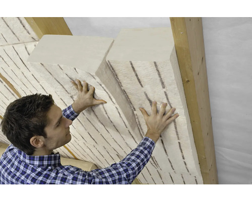 Un homme installe des matériaux d''isolation entre les chevrons du toit pour l''isolation thermique.