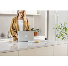 Frau arbeitet am Laptop in der Küche, wo sich auch eine Überwachungskamera befindet