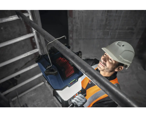 Arbeiter mit Schutzhelm befestigt eine Akku-Baustellenleuchte an einem Rohr.