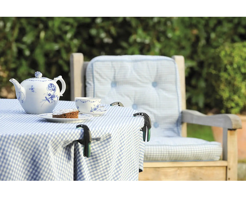 Table de jardin dressée avec théière, tasse, gâteau et pinces à nappe sur une nappe à carreaux à côté d''une chaise avec des coussins