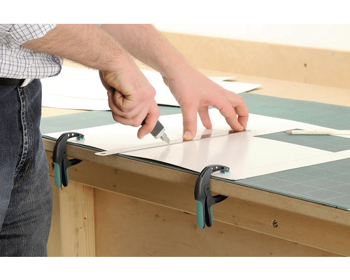 Découpe d''une plaque en plastique avec un cutter et une règle, fixée avec une pince.