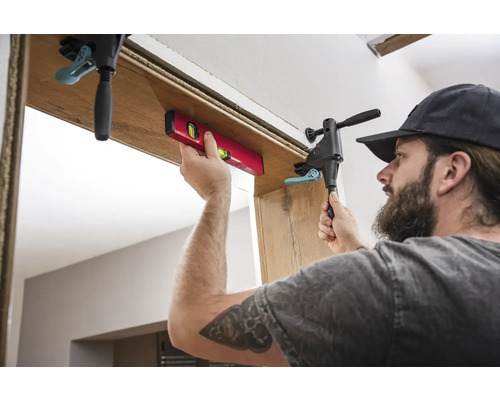 Un artisan monte un chambranle de porte à l''aide d''un niveau à bulle et d''un serre-joint.