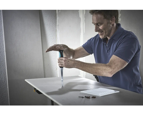 Un homme scie une plaque de plâtre avec une scie sur un établi.