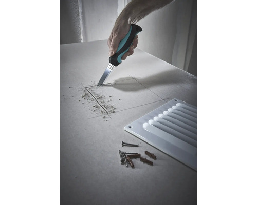 Un artisan est en train de scier un trou dans une plaque de plâtre avec une scie à plaques de plâtre, à côté d''une grille de ventilation ainsi que des vis et des chevilles.