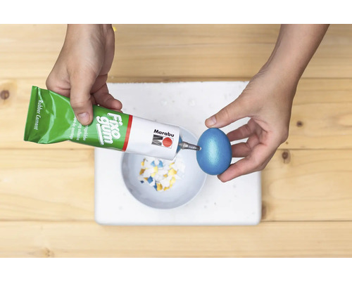 Eine Person klebt Dekorationen mit Klebstoff auf ein Osterei.