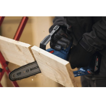 Une tronçonneuse à batterie coupe une planche de bois. Logo Bosch.