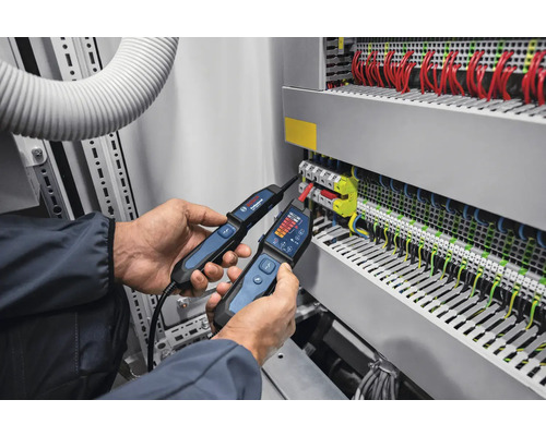 Un électricien utilise deux testeurs de tension sur une armoire électrique pour des mesures électriques.