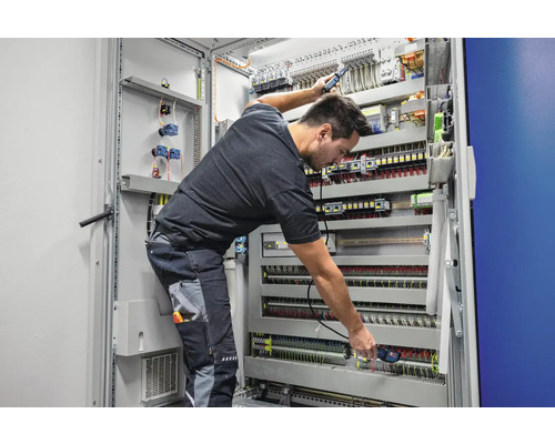 Électricien travaillant sur une boîte de distribution avec des composants électriques, des câbles et du câblage.