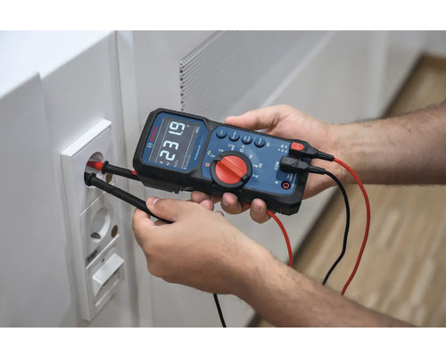 Un homme mesure la tension d'une prise électrique avec un multimètre numérique.