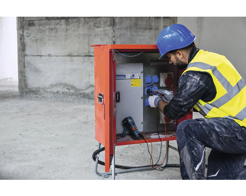 Électricien travaillant sur un poste de distribution électrique sur un chantier.