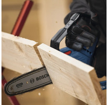 Une personne scie une planche de bois avec une tronçonneuse sans fil. Logo Bosch.