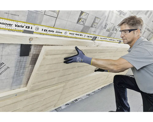 Un homme installe un panneau isolant en fibres de bois sur un mur avec un film pare-vapeur. L''image montre le processus d''isolation thermique dans l''aménagement intérieur.