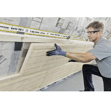 Un homme installe un panneau d''isolation en fibres de bois sur un mur avec un pare-vapeur. Un instrument de mesure est posé dessus.
