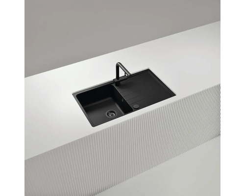 Schwarze Küchenspüle mit Abtropffläche und Armatur in einer hellen Arbeitsplatte