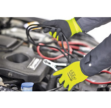 Une personne connecte une batterie de voiture avec des câbles de démarrage, tout en portant des gants.