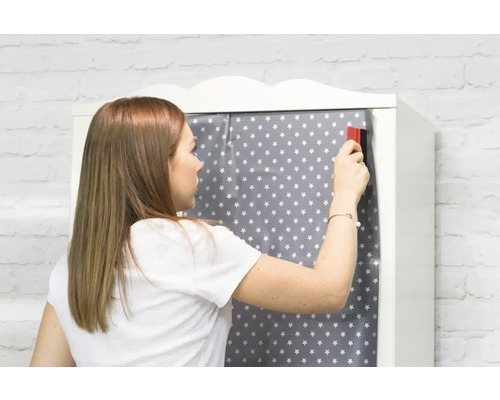 Une femme applique un film décoratif à motif étoilé sur une armoire