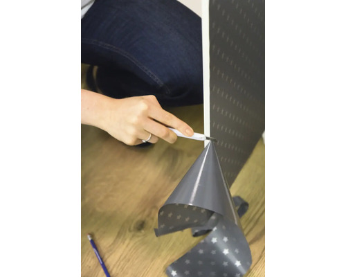 Une personne coupe du papier peint avec un cutter.
