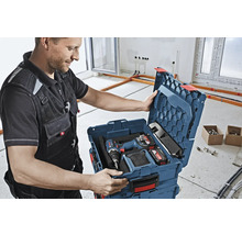 Artisan ouvrant une boîte à outils contenant une visseuse sans fil, des batteries et un chargeur