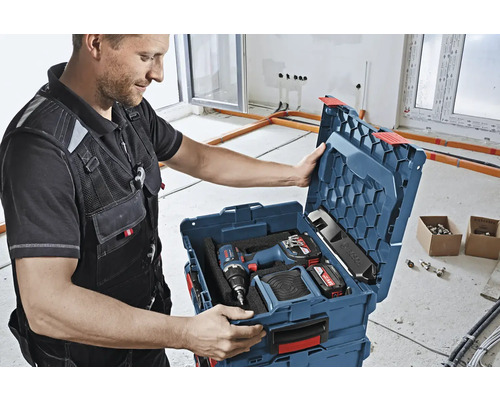 Artisan ouvrant une boîte à outils contenant une visseuse sans fil, des batteries et un chargeur