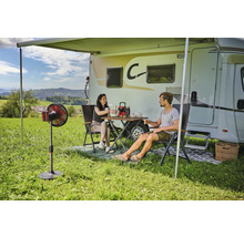 Scène avec camping-car, store, table, chaises et personnes sur une pelouse.