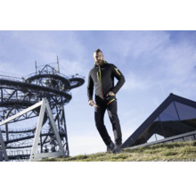 Un homme porte une veste softshell et un pantalon devant une tour d''observation et un bâtiment