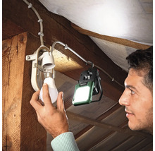 Une personne visse une ampoule dans un plafonnier. Une lampe de chantier fournit un éclairage supplémentaire.