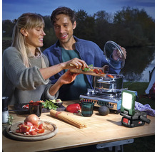 Scène d''extérieur : un couple cuisine sur une table avec un réchaud à gaz et une lampe de travail sans fil.