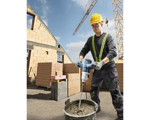 Un ouvrier du bâtiment mélange du mortier avec un malaxeur électrique sur un chantier.