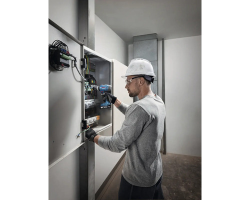 Électricien travaillant avec une visseuse sans fil sur une boîte de distribution.