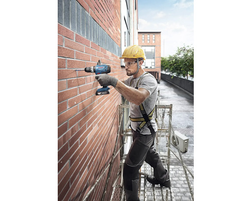 Un artisan perce un trou dans un mur en briques avec une perceuse-visseuse sans fil